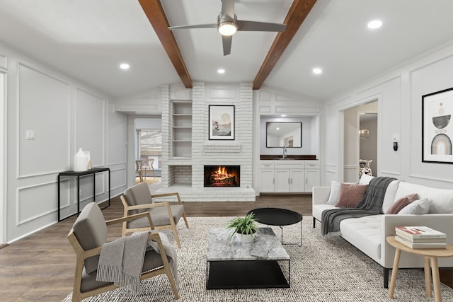 living room featuring lofted ceiling with beams, wood-type flooring, a brick fireplace, and ceiling fan