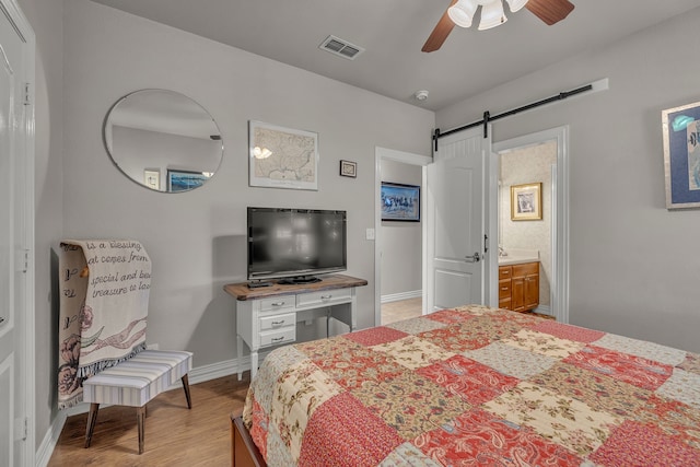 bedroom with a barn door, ensuite bath, ceiling fan, and light hardwood / wood-style flooring