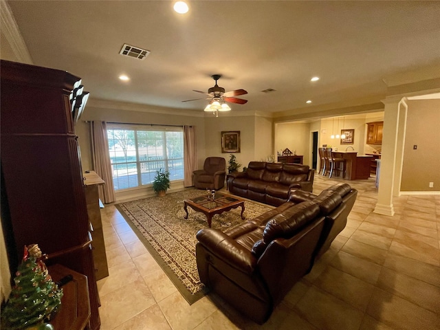 tiled living room with decorative columns, crown molding, and ceiling fan