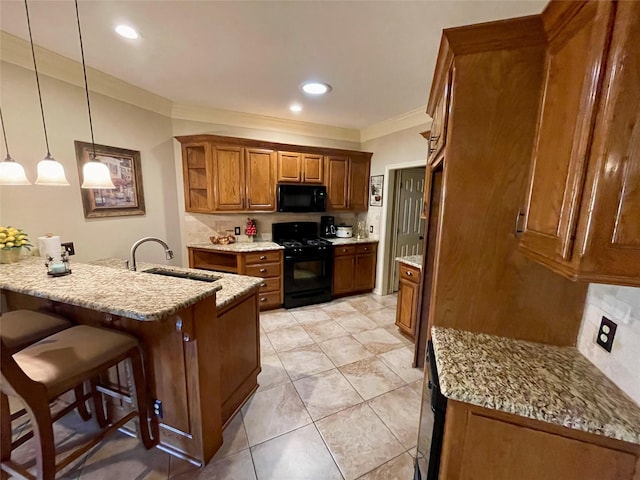 kitchen featuring a breakfast bar, sink, hanging light fixtures, light stone counters, and black appliances