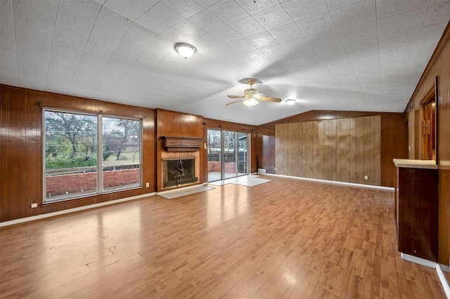 unfurnished living room featuring vaulted ceiling, plenty of natural light, light hardwood / wood-style floors, and wood walls