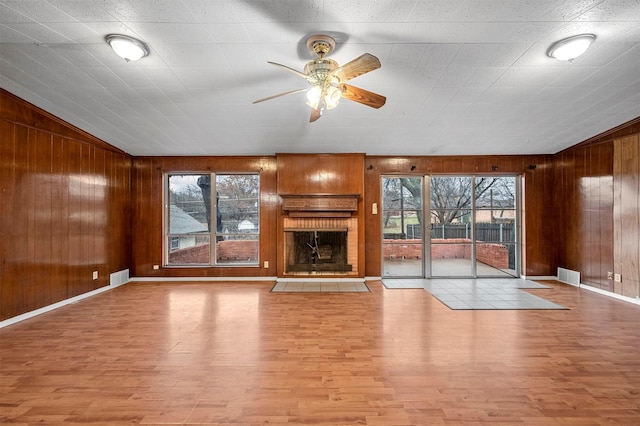 unfurnished living room with wood walls, vaulted ceiling, a brick fireplace, and light wood-type flooring