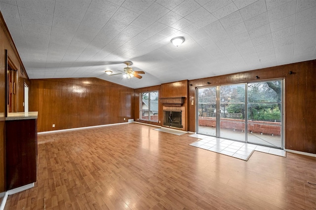 unfurnished living room featuring lofted ceiling, ceiling fan, wooden walls, a large fireplace, and light wood-type flooring