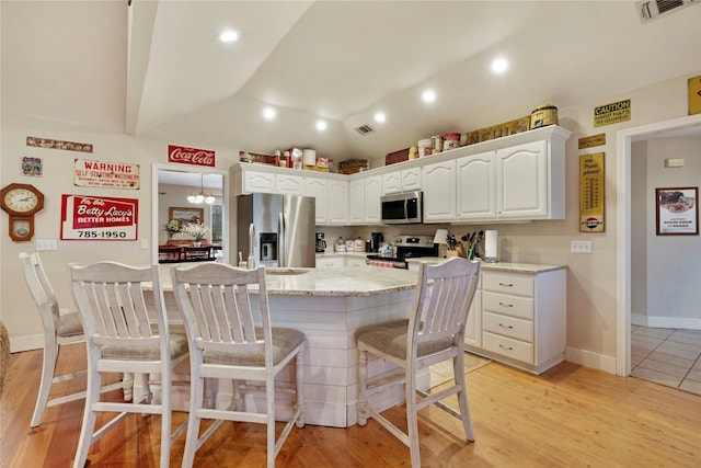 kitchen with lofted ceiling, a breakfast bar, appliances with stainless steel finishes, a kitchen island, and white cabinets