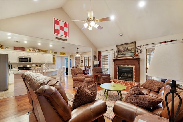 living room featuring ceiling fan, high vaulted ceiling, a fireplace, and light hardwood / wood-style floors