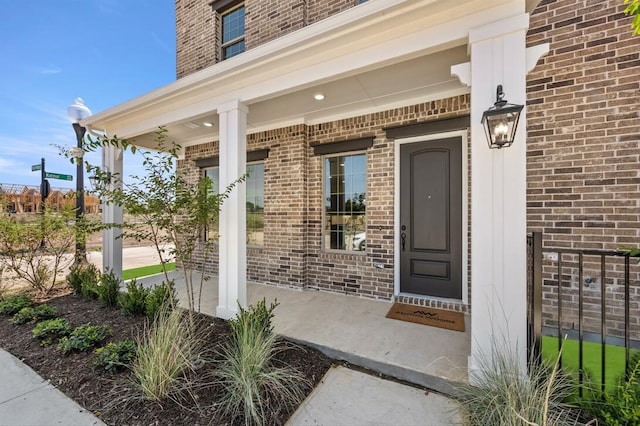 doorway to property with a porch and brick siding