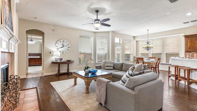 living area with visible vents, arched walkways, a healthy amount of sunlight, a fireplace, and ceiling fan with notable chandelier