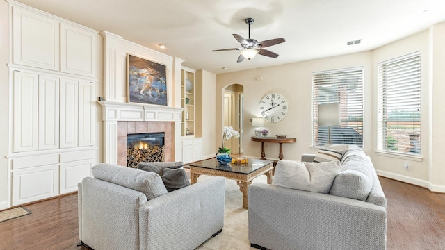 living room featuring ceiling fan, built in features, a fireplace, and light wood-type flooring