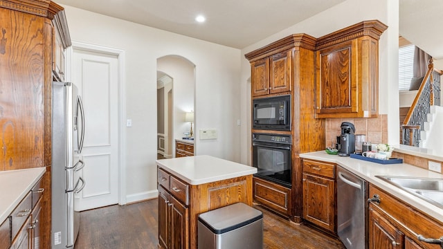 kitchen with sink, dark wood-type flooring, black appliances, a kitchen island, and decorative backsplash