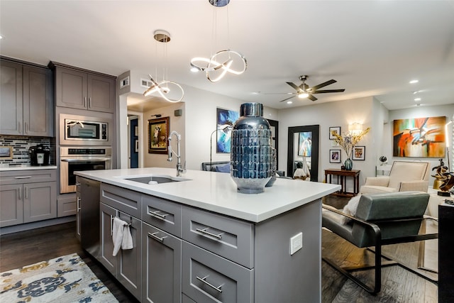 kitchen featuring dark wood-type flooring, sink, decorative light fixtures, appliances with stainless steel finishes, and an island with sink