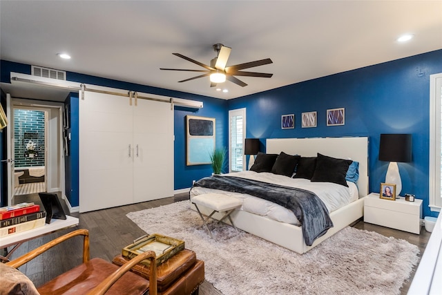 bedroom featuring a barn door, dark wood-type flooring, and ceiling fan