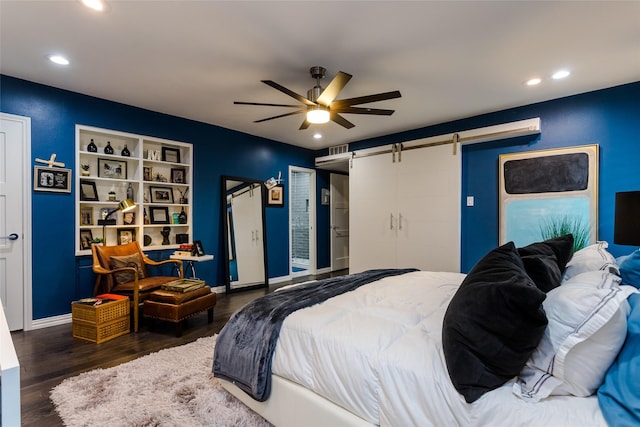 bedroom with ceiling fan, a barn door, and dark hardwood / wood-style flooring