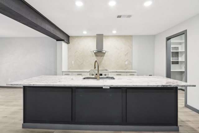 kitchen with sink, light stone countertops, wall chimney range hood, light wood-type flooring, and a spacious island