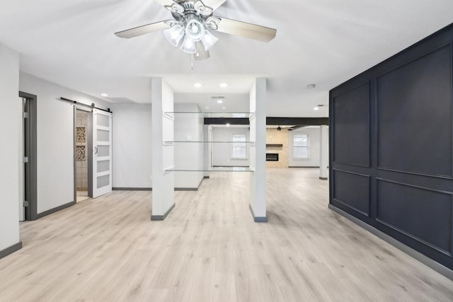 unfurnished living room with ceiling fan, a barn door, light hardwood / wood-style floors, and a fireplace