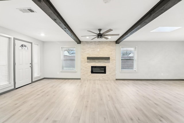 unfurnished living room featuring beamed ceiling, a fireplace, light wood-type flooring, and a wealth of natural light