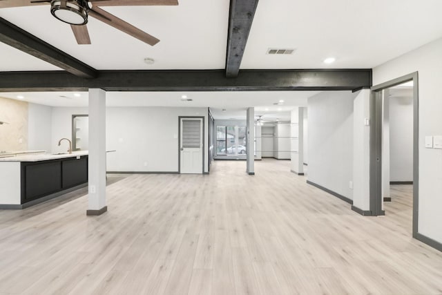 unfurnished living room with beamed ceiling, ceiling fan, sink, and light wood-type flooring