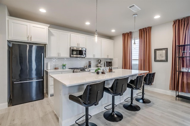 kitchen with a center island with sink, white cabinetry, appliances with stainless steel finishes, and pendant lighting