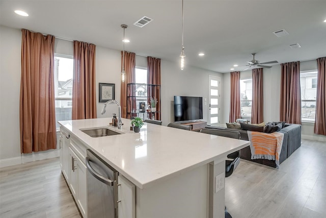 kitchen featuring decorative light fixtures, dishwasher, an island with sink, sink, and white cabinets