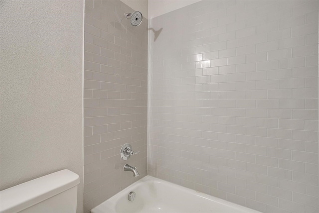 bathroom with tiled shower / bath combo and toilet