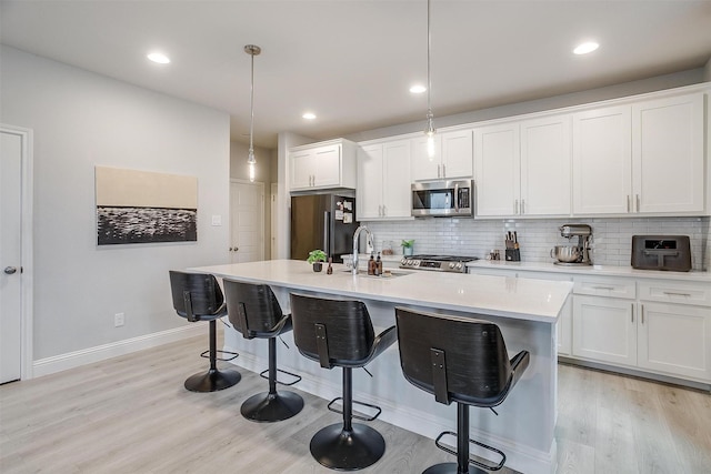 kitchen with pendant lighting, stainless steel appliances, an island with sink, and white cabinets