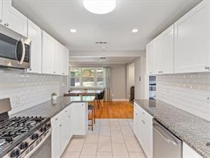 kitchen with dark stone countertops, tasteful backsplash, stainless steel appliances, and white cabinets