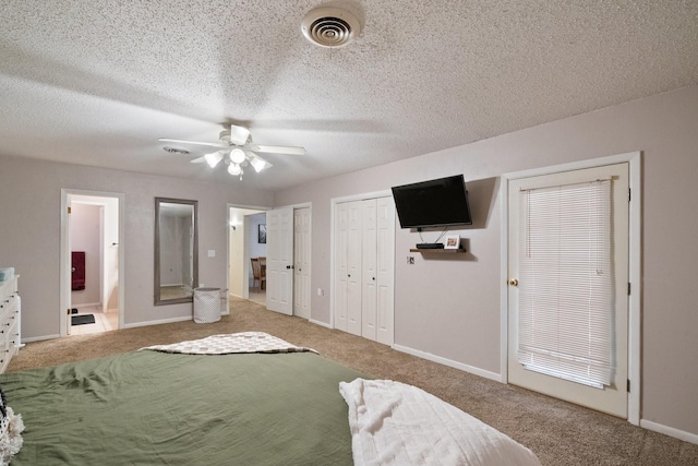 carpeted bedroom featuring ensuite bathroom, ceiling fan, a textured ceiling, and two closets