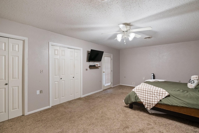 bedroom with ceiling fan, two closets, carpet flooring, and a textured ceiling