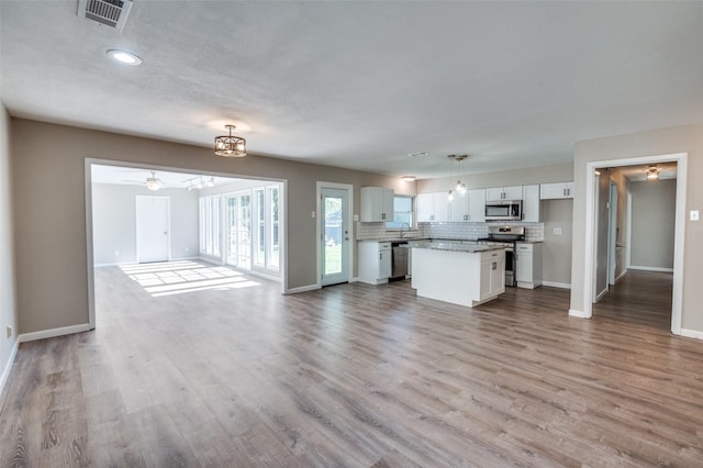 unfurnished living room featuring ceiling fan with notable chandelier, light hardwood / wood-style flooring, and a textured ceiling