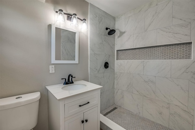 bathroom with tiled shower, vanity, and toilet