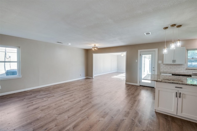 kitchen featuring light stone counters, decorative light fixtures, white cabinets, light hardwood / wood-style floors, and backsplash