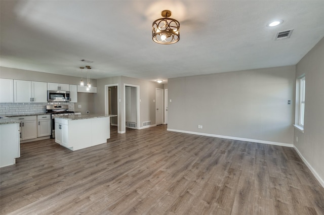 kitchen with a center island, hanging light fixtures, appliances with stainless steel finishes, light stone countertops, and white cabinets