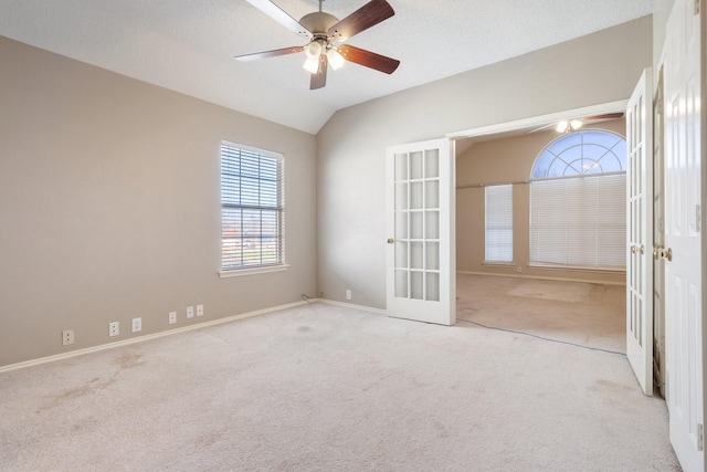 carpeted spare room with a textured ceiling, vaulted ceiling, french doors, and ceiling fan