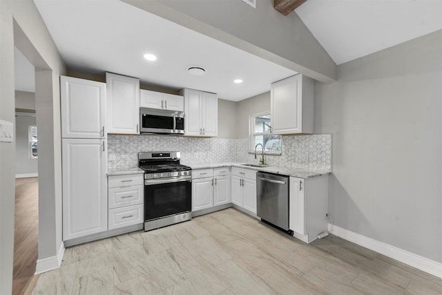 kitchen with appliances with stainless steel finishes, sink, white cabinets, backsplash, and light stone countertops