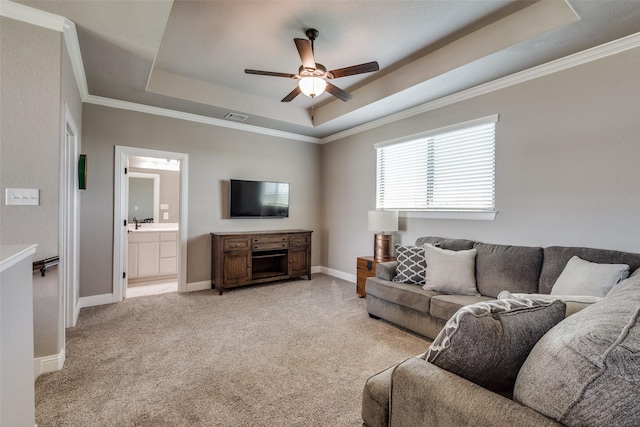 living room with a tray ceiling, ornamental molding, light colored carpet, and ceiling fan