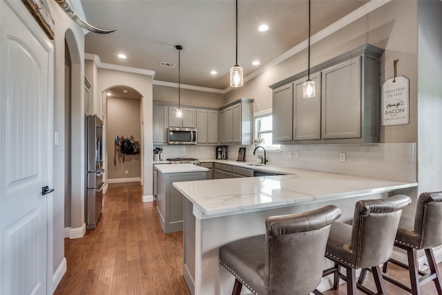 kitchen featuring a kitchen bar, decorative light fixtures, kitchen peninsula, gray cabinets, and stainless steel appliances