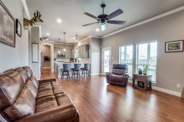 living room with hardwood / wood-style flooring, ceiling fan, ornamental molding, and a textured ceiling