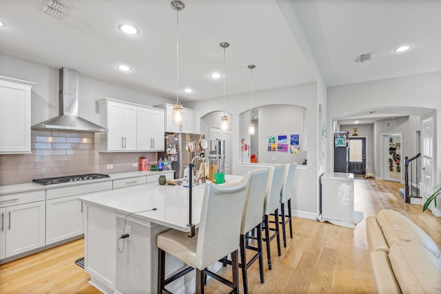 kitchen with pendant lighting, wall chimney exhaust hood, a center island with sink, and white cabinets