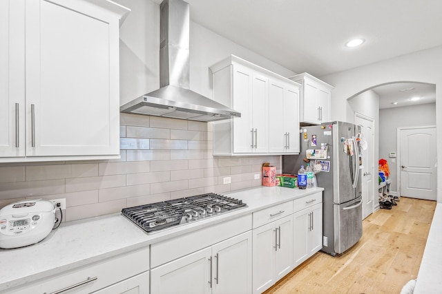 kitchen with appliances with stainless steel finishes, white cabinetry, tasteful backsplash, light hardwood / wood-style floors, and wall chimney exhaust hood