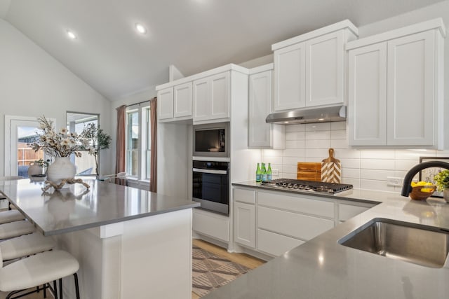 kitchen featuring lofted ceiling, a kitchen bar, sink, stainless steel appliances, and white cabinets