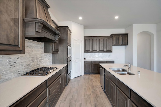 kitchen with dark brown cabinetry, sink, stainless steel appliances, and custom range hood