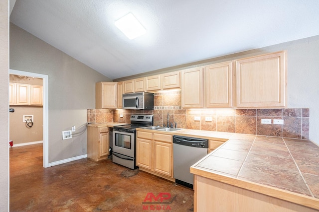 kitchen featuring vaulted ceiling, tile countertops, sink, backsplash, and stainless steel appliances