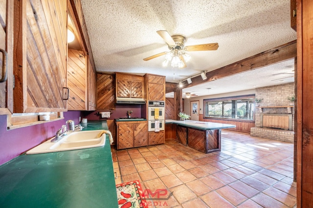 kitchen featuring sink, light tile patterned floors, double oven, a textured ceiling, and kitchen peninsula