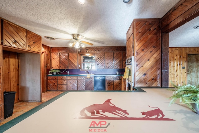 kitchen with wooden walls, sink, ceiling fan, stainless steel appliances, and a textured ceiling