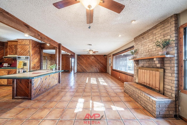 kitchen with wooden walls, a breakfast bar area, double wall oven, a brick fireplace, and a textured ceiling