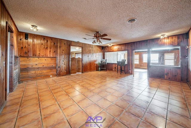 interior space featuring light tile patterned floors, a textured ceiling, wooden walls, and ceiling fan