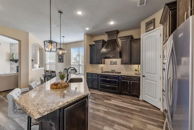 kitchen with stainless steel appliances, an island with sink, custom exhaust hood, and a kitchen breakfast bar