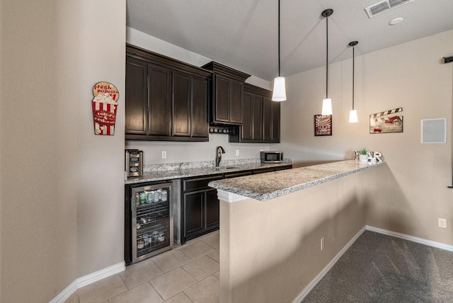 bar featuring wine cooler, dark brown cabinetry, sink, hanging light fixtures, and light stone countertops