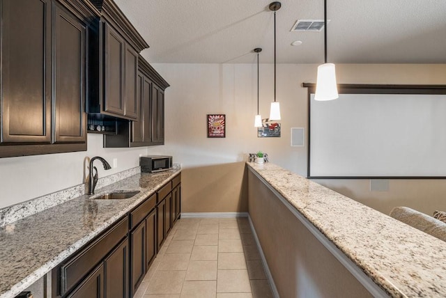 kitchen with pendant lighting, sink, light tile patterned floors, light stone countertops, and dark brown cabinets