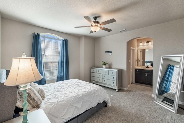 bedroom featuring sink, ensuite bath, light carpet, a textured ceiling, and ceiling fan