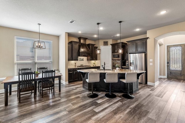 kitchen featuring decorative light fixtures, an island with sink, sink, stainless steel appliances, and dark brown cabinets